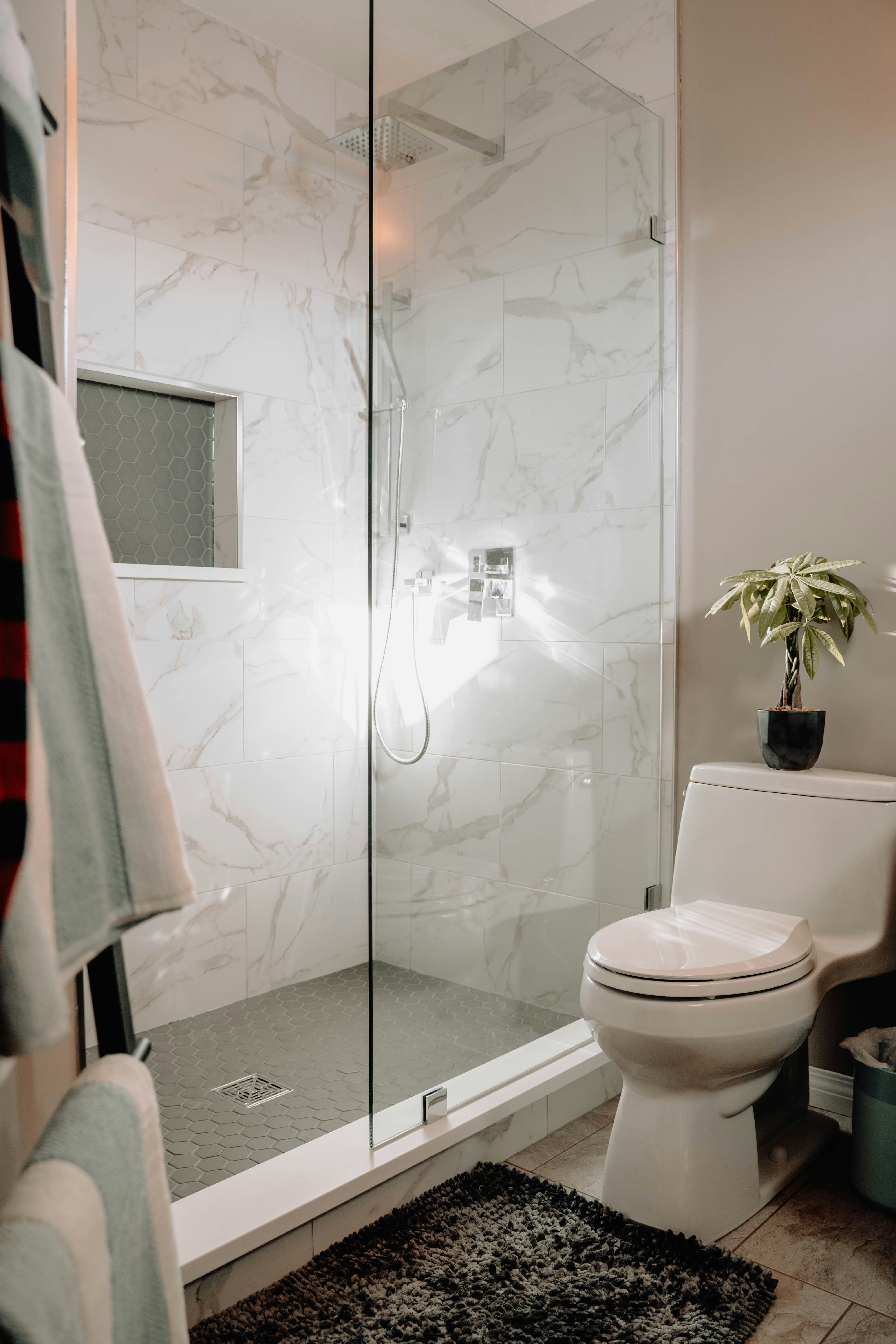 Frameless glass shower with marble-look tile walls and hexagon mosaic floor, toilet in foreground